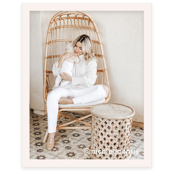 Woman wearing an all-white outfit and taupe leather Starling flats while holding a baby 